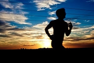 Image shows the silhouette of a runner against the setting sun. 