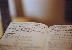 Image shows a notebook with mathematical formulae written in it.