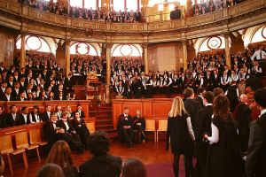 Image shows the Sheldonian Theatre full of Oxford students in academic dress.