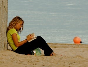 Image shows a young woman reading on a beach.
