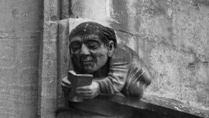 Image shows a stone carving of a man reading a book. 