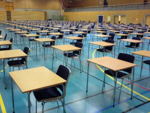 Image shows rows of empty desks in an exam hall. 