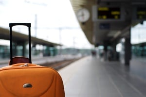 Image shows an orange suitcase on a railway station platform.