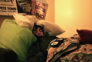 Image shows a student asleep in a pile of cushions and duvets.