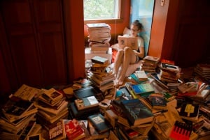 Image shows a girl reading a book, surrounded by stacks and stacks of other books.