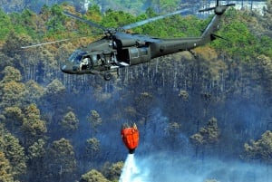 Image shows an army fire helicopter spreading water onto a forest fire.