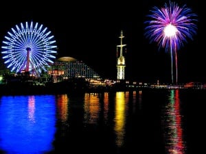 Image shows fireworks going off, over a river, near a Ferris wheel.