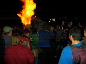 Image shows a man carrying a blazing tar barrel through a crowd.