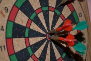 Image shows a dartboard with darts clustered around the bullseye.