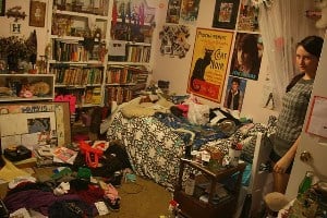 Image shows a teenager standing in the doorway of an incredibly messy room.