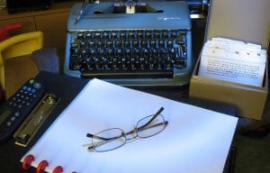 Image shows an assortment of writing tools, including a notebook and typewriter.