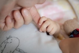Image shows a baby holding an adult's finger.