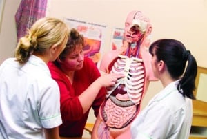 Image shows a nurse talking to two medical students. 