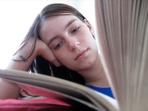 Image shows a young woman reading a book. 
