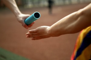 Image shows a baton being passed between runners.