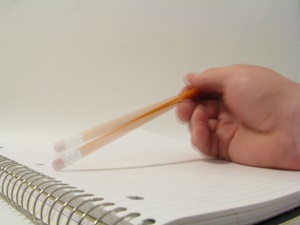 Image shows someone tapping a yellow pencil on a blank page.