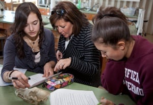 Image shows a woman with her two daughters on either side of her, reading an essay that one of them is presenting to her.